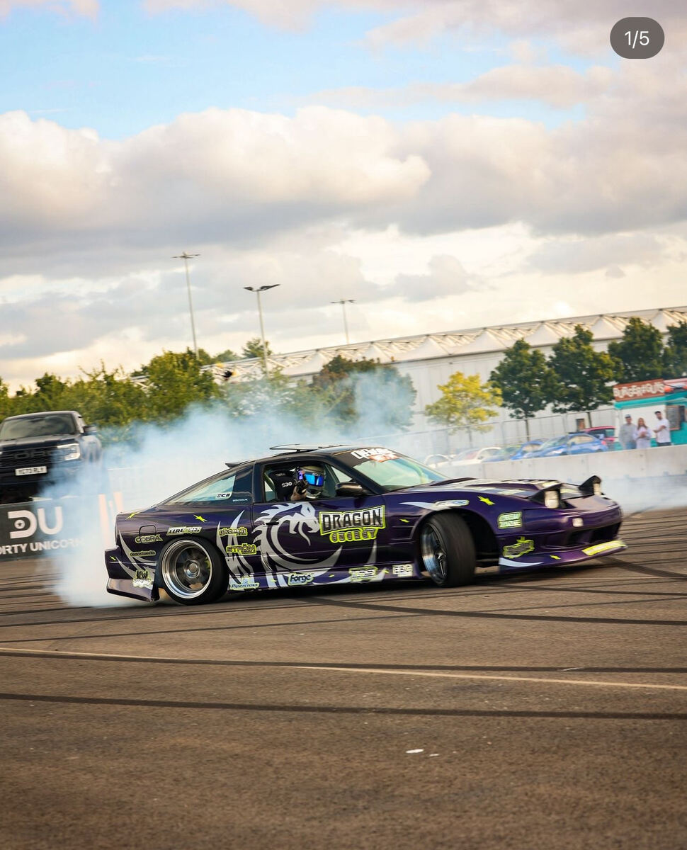 Dragon Energy branded drift car performing a burnout at a motorsport event
